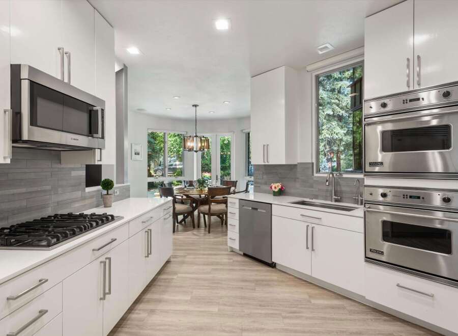 Experience modern luxury in this stunning kitchen, featuring sleek white cabinetry, a sophisticated grey tile backsplash, and high-end stainless steel appliances including a Bosch microwave and Viking double ovens.