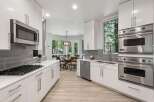 Experience modern luxury in this stunning kitchen, featuring sleek white cabinetry, a sophisticated grey tile backsplash, and high-end stainless steel appliances including a Bosch microwave and Viking double ovens.