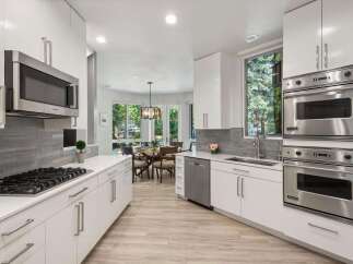 Experience modern luxury in this stunning kitchen, featuring sleek white cabinetry, a sophisticated grey tile backsplash, and high-end stainless steel appliances including a Bosch microwave and Viking double ovens.