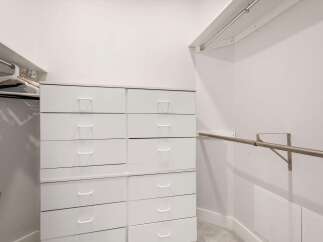 Discover ample storage solutions in this spacious walk-in closet, featuring a sleek white dresser with multiple drawers and a convenient hanging rod.