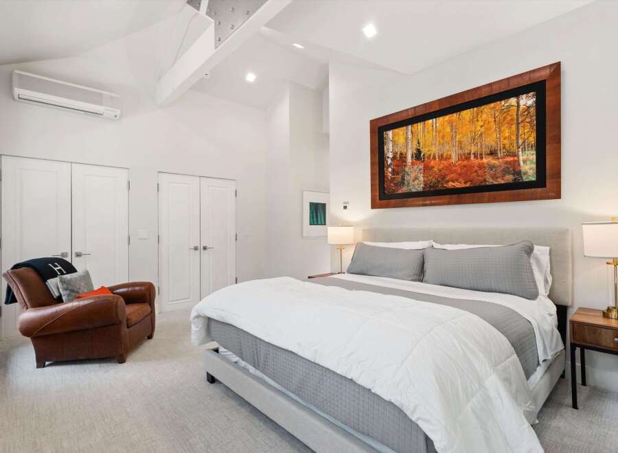 Experience luxury in this stunning bedroom featuring a king-sized bed with plush grey bedding and a cozy leather armchair.