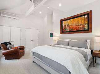 Experience luxury in this stunning bedroom featuring a king-sized bed with plush grey bedding and a cozy leather armchair.