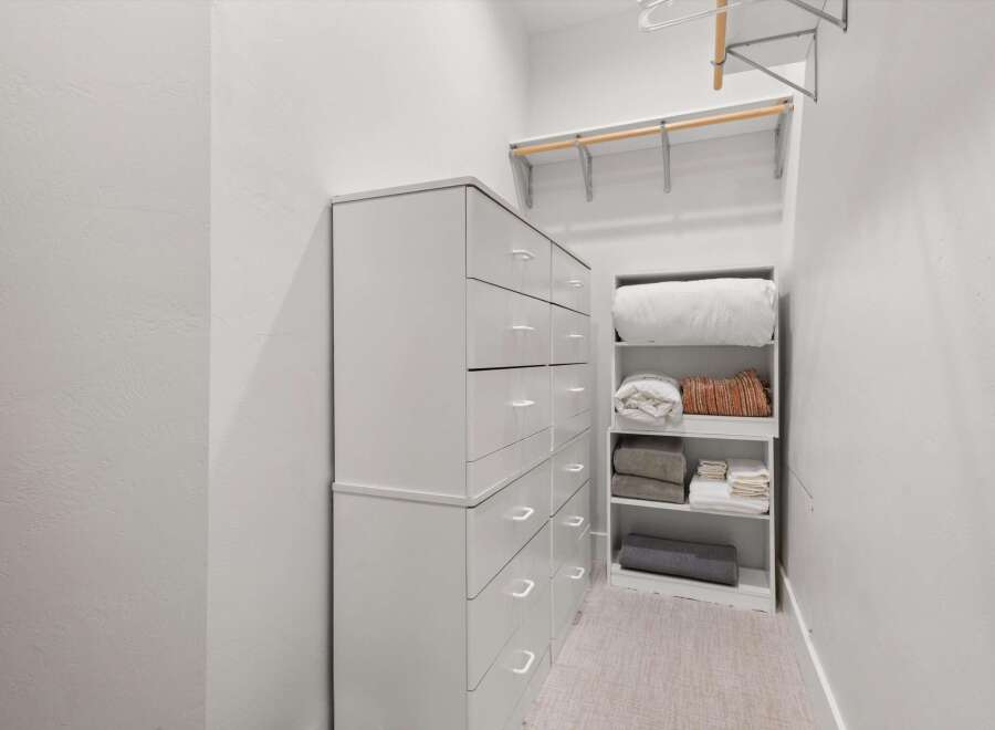 Discover ample storage solutions in this well-organized closet, featuring a tall chest of drawers and a dedicated shelving unit.