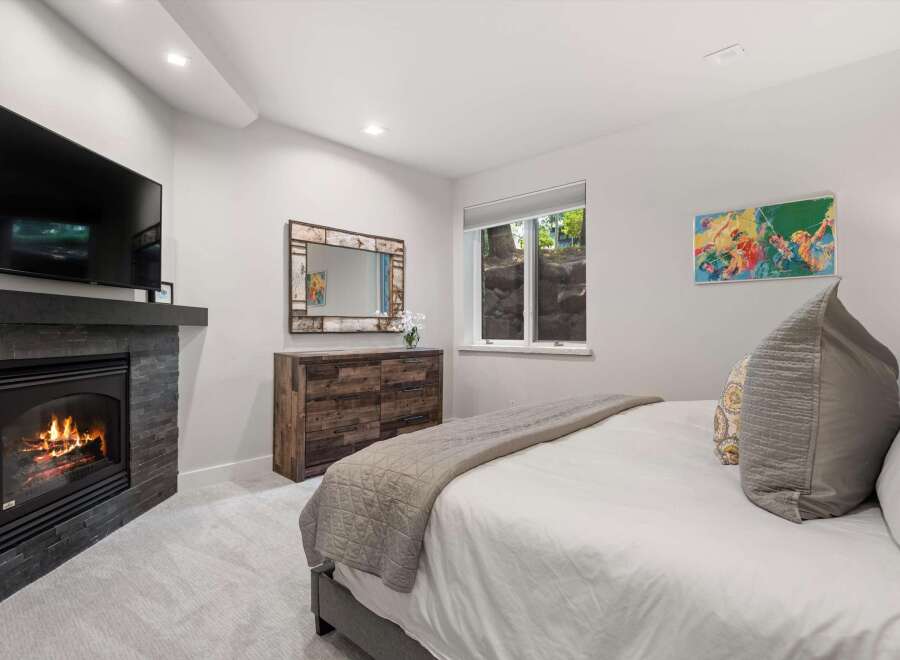 Experience ultimate comfort in this master bedroom, featuring a modern gas fireplace with a stone surround and a wall-mounted television.