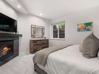 Experience ultimate comfort in this master bedroom, featuring a modern gas fireplace with a stone surround and a wall-mounted television.