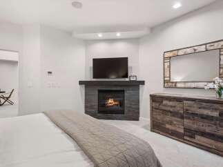 Experience ultimate comfort in this master bedroom, featuring a cozy gas fireplace and a mounted flat-screen TV for entertainment.