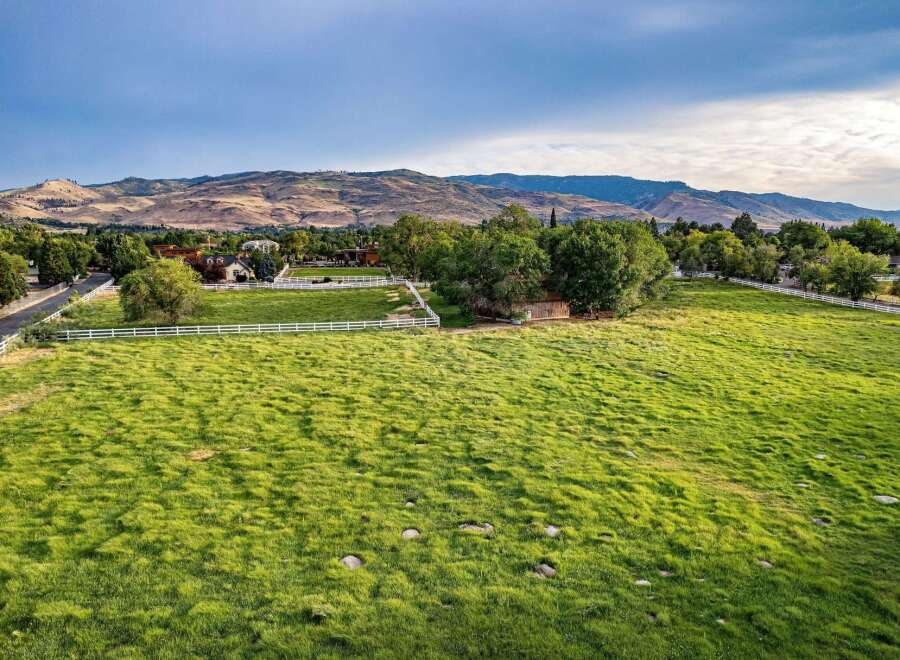 Experience the serene beauty of this expansive rural property, featuring lush green pastures bordered by a classic white fence.