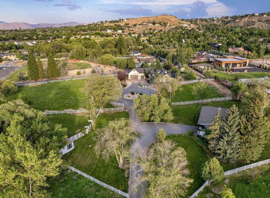 Discover this expansive estate featuring a charming main residence with a spacious driveway and a detached garage, all set against a backdrop of rolling hills and mature trees.