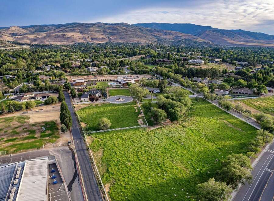 Discover this expansive property featuring a charming home with a circular driveway and a white fence surrounding a lush green lawn.