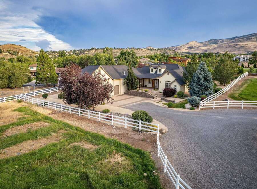 Discover this stunning property featuring a charming cream-colored home with a dark roof, nestled amidst lush greenery and rolling hills.