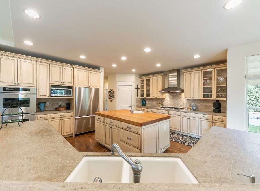 This spacious kitchen boasts custom cream-colored cabinetry with glass-front upper cabinets, complemented by a large butcher block island with a sink.