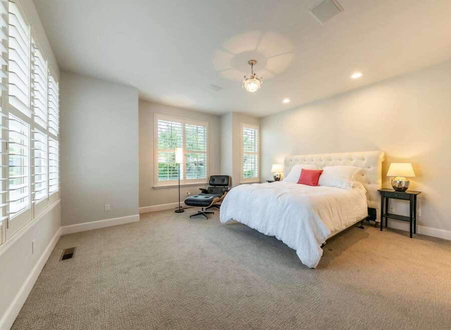 Experience ultimate comfort in this luxurious bedroom, featuring a plush white duvet, a striking tufted headboard, and a vibrant coral accent pillow.