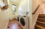 This spacious laundry room features a side-by-side washer and dryer set, ample white cabinetry for storage, and a large window offering natural light.