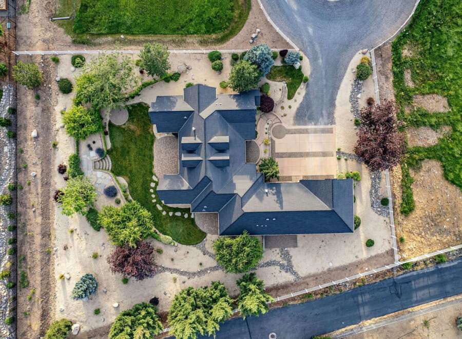 Discover this stunning aerial view of a luxurious estate, showcasing its expansive dark-shingled roofline and meticulously landscaped grounds.