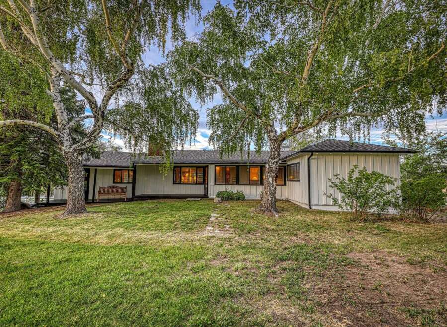 Nestled amongst mature trees, this charming home offers a serene retreat with its classic white siding and large windows that invite natural light.