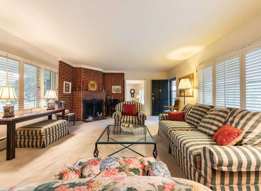 Step into this inviting living room, featuring a charming brick fireplace and ample natural light from plantation shutters.
