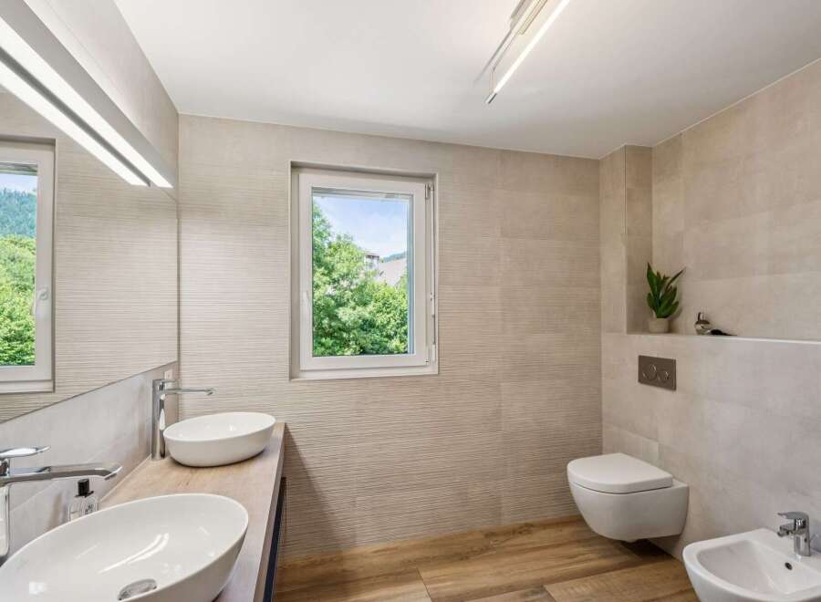 Experience modern luxury in this stunning bathroom featuring dual vessel sinks atop a sleek wooden vanity, complemented by a wall-mounted toilet and a matching bidet.
