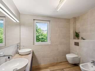 Experience modern luxury in this stunning bathroom featuring dual vessel sinks atop a sleek wooden vanity, complemented by a wall-mounted toilet and a matching bidet.