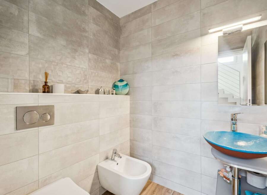 This modern bathroom features a sleek design with large format tiles on the walls and a unique blue vessel sink.