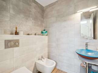 This modern bathroom features a sleek design with large format tiles on the walls and a unique blue vessel sink.