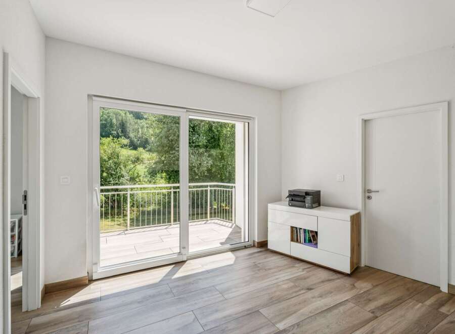 Step into this bright and airy room, featuring a large sliding glass door that opens to a balcony with a scenic view of lush greenery.