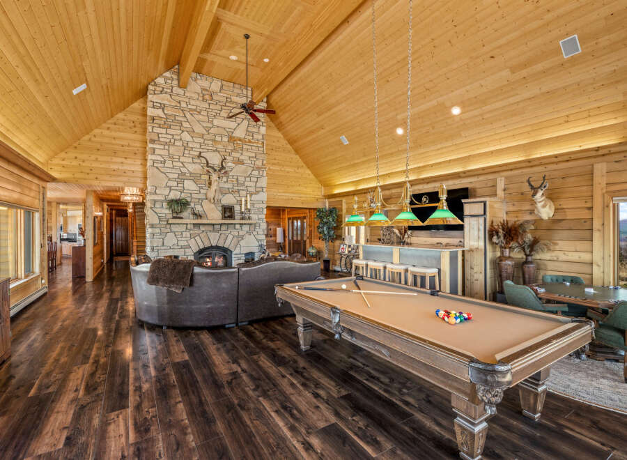Experience ultimate relaxation and entertainment in this stunning log cabin living space, featuring a grand stone fireplace and a spacious seating area perfect for gatherings.