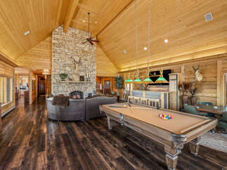 Experience ultimate relaxation and entertainment in this stunning log cabin living space, featuring a grand stone fireplace and a spacious seating area perfect for gatherings.