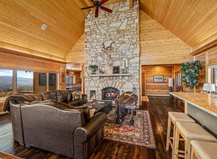 Experience rustic luxury in this stunning mountain lodge living room, featuring a grand stone fireplace and vaulted wood-paneled ceilings.