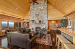 Experience rustic luxury in this stunning mountain lodge living room, featuring a grand stone fireplace and vaulted wood-paneled ceilings.