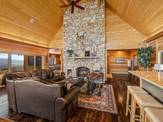 Experience rustic luxury in this stunning mountain lodge living room, featuring a grand stone fireplace and vaulted wood-paneled ceilings.