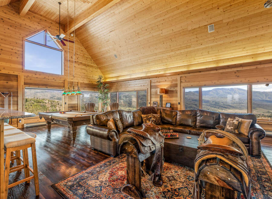 Experience rustic luxury in this stunning mountain lodge featuring a spacious living area with a large leather sectional and a pool table.