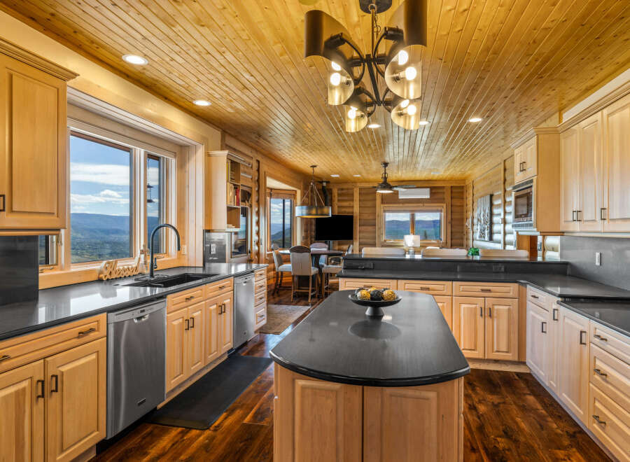Experience breathtaking mountain views from this stunning kitchen, featuring elegant light wood cabinetry and sleek black countertops.
