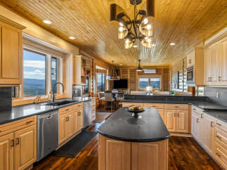 Experience breathtaking mountain views from this stunning kitchen, featuring elegant light wood cabinetry and sleek black countertops.