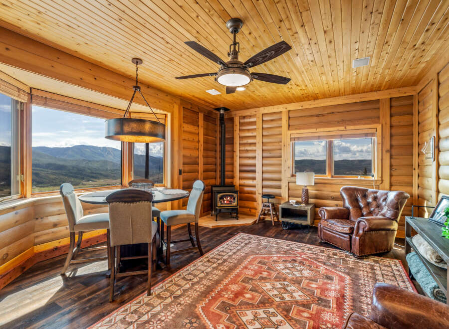 Experience cozy living in this charming log cabin featuring a rustic dining area with mountain views and a wood-burning stove for warmth.