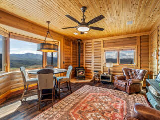 Experience cozy living in this charming log cabin featuring a rustic dining area with mountain views and a wood-burning stove for warmth.