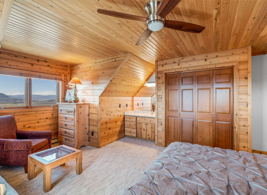 Experience rustic charm in this cozy bedroom featuring warm wood paneling throughout and a vaulted ceiling with a ceiling fan.
