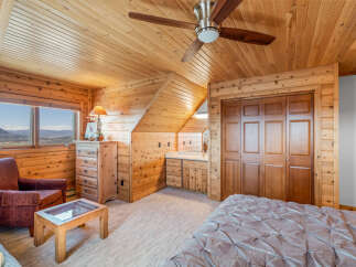 Experience rustic charm in this cozy bedroom featuring warm wood paneling throughout and a vaulted ceiling with a ceiling fan.