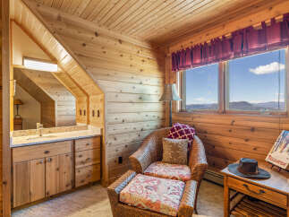 Experience rustic charm in this wood-paneled room featuring a cozy wicker chair with patterned cushions and a view of the mountains.
