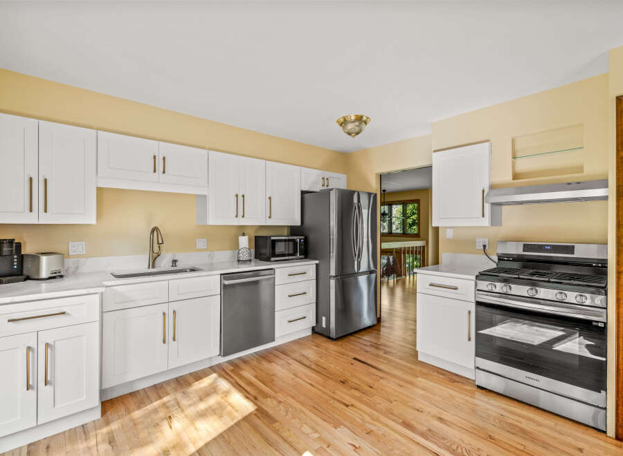 This kitchen boasts modern white cabinetry with elegant brass hardware, complemented by sleek quartz countertops.