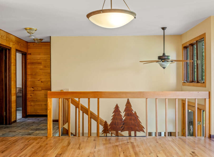 This charming interior features warm wood paneling and a beautiful wooden staircase with a unique tree silhouette design.