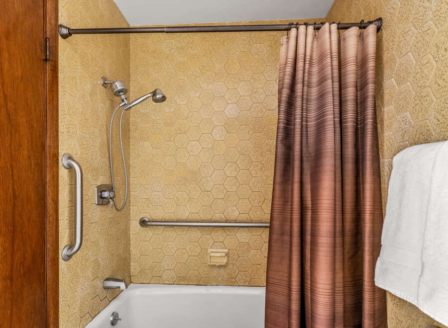 This accessible bathroom features a bathtub with a showerhead, grab bars for safety, and a convenient soap dish.