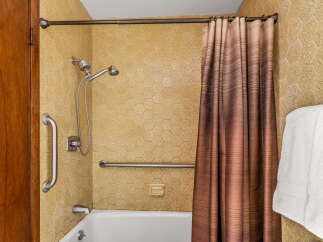 This accessible bathroom features a bathtub with a showerhead, grab bars for safety, and a convenient soap dish.