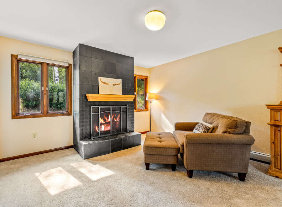Cozy up by the inviting fireplace in this charming living room, featuring a striking black tile surround and a warm wooden mantel.