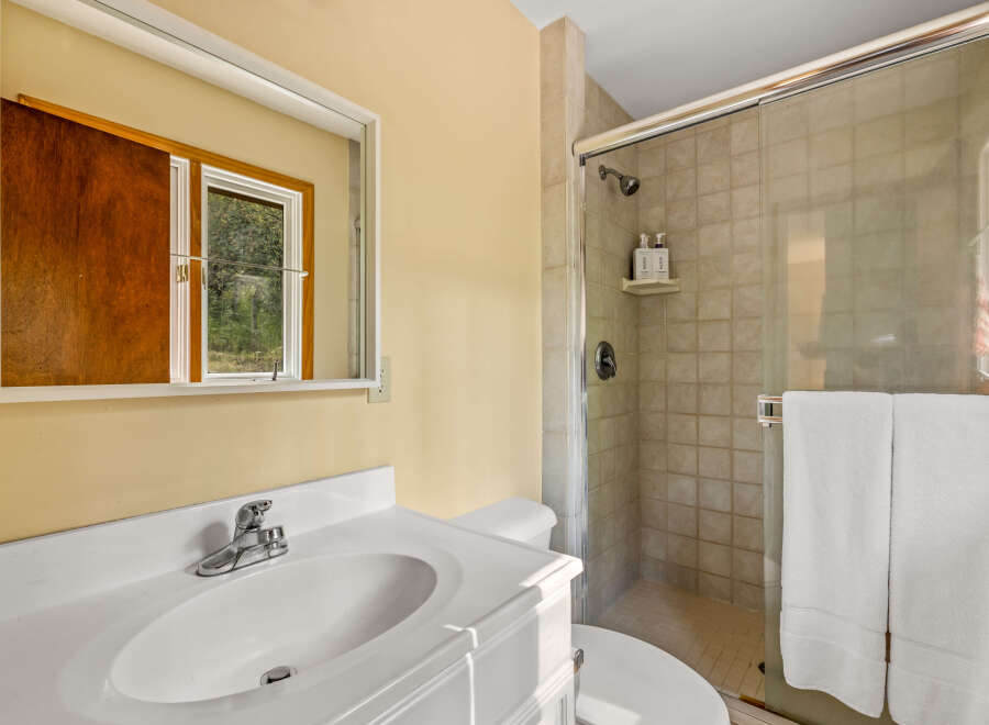This bathroom features a clean white vanity with a sink and chrome faucet, complemented by a large mirror reflecting a window with a wooded view.
