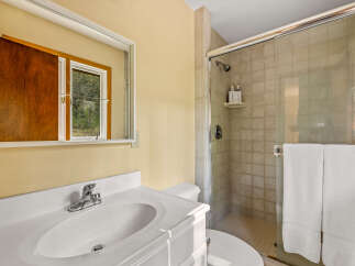 This bathroom features a clean white vanity with a sink and chrome faucet, complemented by a large mirror reflecting a window with a wooded view.