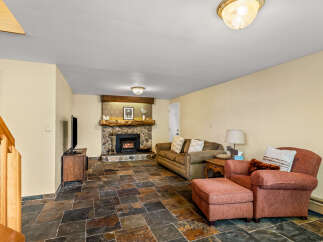 Cozy up by the stone fireplace in this inviting living room, featuring a comfortable sofa and armchair perfect for relaxation.