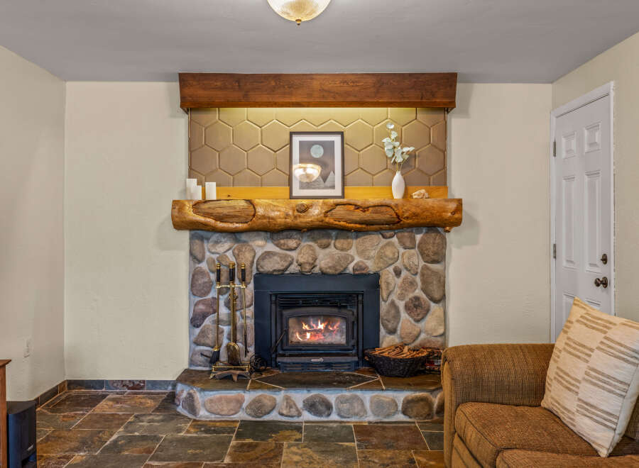 Cozy up by the stone fireplace, featuring a rustic log mantel and a modern insert with a crackling fire.