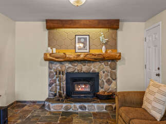 Cozy up by the stone fireplace, featuring a rustic log mantel and a modern insert with a crackling fire.