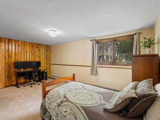 This cozy bedroom features a comfortable bed with decorative pillows, a functional workspace with dual monitors, and a charming wooden dresser.