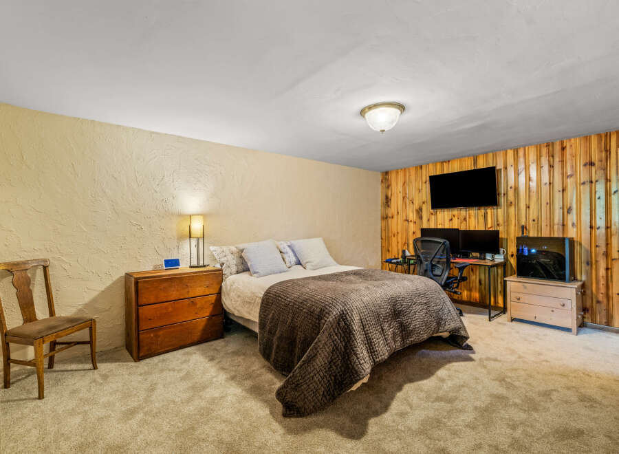 This bedroom offers a cozy retreat with a comfortable bed, a functional workspace with dual monitors, and ample storage.